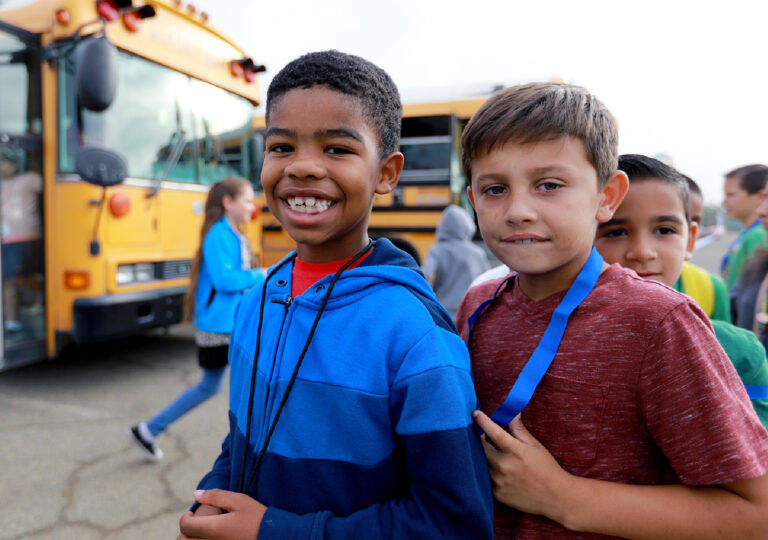 two smiling kids by school busses